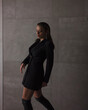 © NASTYA PALEHINA - teen fashion. young girl in black slim dress-jacket and over the knee boots is standing casual in step and looking down with smile on the gray wall background in studio. lifestyle concept, free space