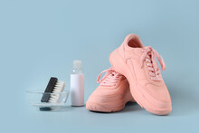 Dirty pink sneakers with brush and special tool for cleaning them on blue background. Concept washing and regular care about sneakers.