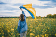 Ukrainian patriot woman waving national flag in canola yellow field. Rare, back view. Ukraine unbreakable, peace, independence, freedom, victory in war.