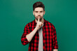 Young serious secret caucasian man he wear red shirt grey t-shirt say hush be quiet with finger on lips shhh gesture isolated on plain dark green background studio portrait People lifestyle concept.