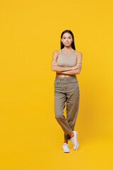 Wall Mural - Full body serious calm attractive young latin woman 30s she wearing beige tank shirt look camera hold hands crossed folded isolated on plain yellow backround studio portrait People lifestyle concept