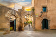 A woman walks through an arched passage on a cobblestone alley in the historic medieval hilltop village of Tossa de Mar on the Costa Brava coast of Spain, at sunset.