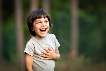 Portrait of adorable little excited boy against green forest outdoors in summer