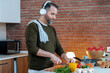 Handsome mature man cutting fresh vegetables while listening music with headphones in the kitchen at home.