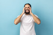© khosrork - Portrait of sick man with beard wearing white T-shirt suffering from terrible headache, frowning face, keeping fingers on temples. Indoor studio shot isolated on blue background.