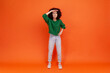 © khosrork - Full length portrait of curious woman with Afro hairstyle wearing green casual style sweater looking far away with hand over head, trying to see. Indoor studio shot isolated on orange background.
