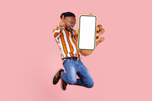 Hey You Look Here. Happy Young Man Flying And Jumping In Air And Showing Big Mobile Empty Screen For Copy Space And Advertising Area. Indoor Studio Shot Isolated On Pink Background