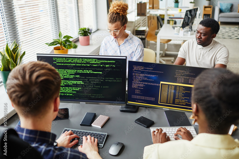 Group of software developers sitting at desk with computer monitors and ...