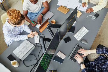 High angle view of group of programmers discussing development of new software sitting at table with computer monitors
