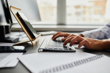close-up of young programmer typing on keyboard to write code of software while sitting in front of 
