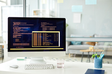 Close-up of workplace of programmer with computer standing on it with codes on monitor at office