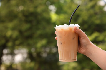 Wall Mural - Woman holding plastic takeaway cup of delicious iced coffee outdoors, closeup. Space for text