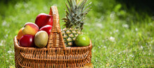 Wicker Basket With Fresh Fruits On Green Grass Outdoors