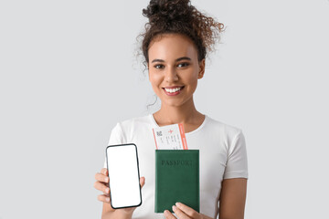 Sticker - Female African-American tourist with mobile phone and passport on light background