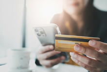 Online Payment, Woman's Hands Holding A Credit Card And Using Smart Phone For Online Shopping On Blurred Background.