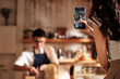 © DragonImages - Young woman filming video of barista making coffee for social media account of coffeeshop, selective focus