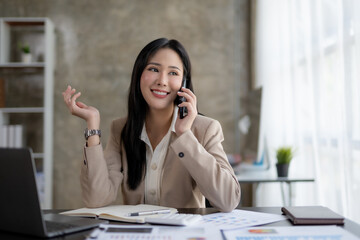 Wall Mural - Happy young Asian business woman talking on the phone in the office.