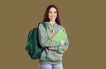 Wall Mural - Portrait of high school, college or university student with books and backpack. Happy young woman or teenage girl in casual clothes standing isolated on brown background, holding notebooks and smiling