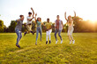 canvas print picture - Group of several happy excited cheerful young diverse friends meeting up on warm sunny day in summer, spending time outside, having fun, and jumping on green field, meadow or park lawn all together