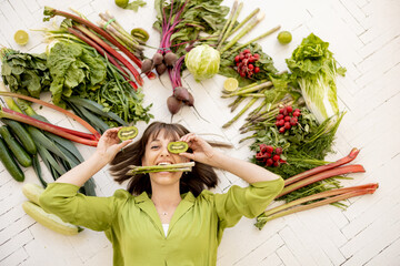 Portrait of a young cheerful woman with lots of fresh vegetables, fruits and greens above her head, top view. Concept of vegan food and healthy lifestyle