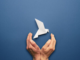 Wall Mural - Hands protecting an origami peace dove on a blue paper background, freedom cocnept