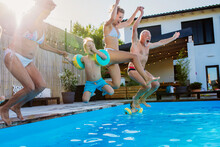 Generation Family Having Fun Together When Jumping Into The Swimming Pool At Backyard.