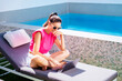 Woman sitting on a lounger by the pool and using a laptop