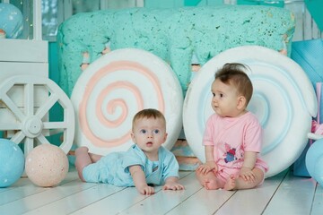 A two baby lies on a soft surface in a bright room, dressed in blue and pink clothing. The concept of childhood and baby care.