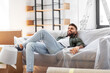 canvas print picture - moving, people and real estate concept - happy smiling man with boxes resting on sofa covered with plastic sheeting at new home