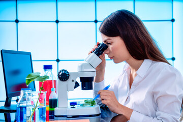 Wall Mural - Young woman with microscope in GMO laboratory. Study of green plant of agricultural plants with a microscope