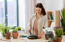 People, Gardening And Housework Concept - Happy Woman With Fork Loosening Soil In Glass Vase And Planting Flowers At Home