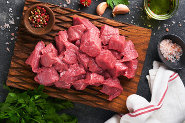 Wall Mural - Raw chopped beef meat. Raw organic meat beef or lamb, spices, herbs on old wooden board on dark grey concrete background. Goulash. Raw uncooked meat. Meat with blood. Top view with copy space.