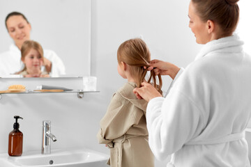 Sticker - beauty, family and people concept - happy smiling mother and daughter looking to mirror and braiding hair in bathroom