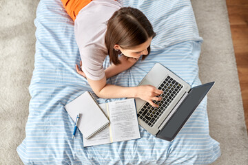 school, online education and e-learning concept - teenage student girl with laptop computer writing to notebook lying on bed at home