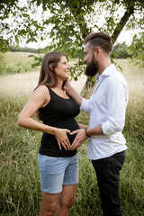 Wall Mural - pretty young pregnant woman with black shirt is standing with her boyfriend in a high meadow and they are happy and full of anticipation for the baby