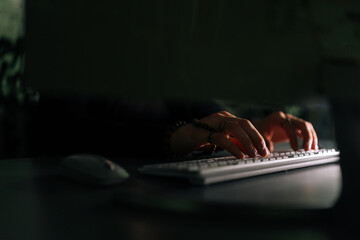 Close-up hands of unrecognizable hacker breaking online web site, engaging hacking into security systems, typing wireless keyboard sitting at desk in dark room. Concept of data thief, internet attack