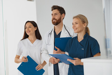 Wall Mural - Portrait of a group of happy doctors and nurses standing near reception in hospital and looking away