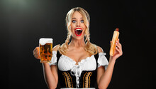 Young Sexy Oktoberfest Girl Waitress, Wearing A Traditional Bavarian Or German Dirndl, Serving Big Beer Mugs With Drink Isolated On Black Background.
