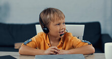 Happy Boy In Headset With Microphone Talking Near Laptop On Desk.