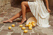 Close up shot of beautiful tanned female legs. Model wearing stylish summer skirt, posing, sitting in street with lemons on the floor
