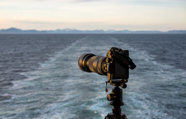 Wall Mural - Professional dslr on tripod on back of cruise ship sailing away from Alaska coast leaving wake