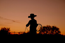 Western Industry Concept With Kid Cowboy Practicing Roping For Rodeo At Sunset In Silhouette On Texas Ranch.