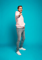 Sticker - Full size photo of smiling brunette man pointing finger at camera isolated on light blue background.