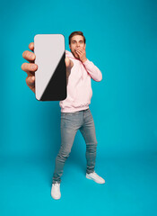 Wall Mural - handsome excited man showing pointing at empty smartphone screen posing over light blue background, 