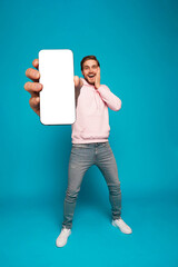 Wall Mural - handsome excited man showing pointing at empty smartphone screen posing over light blue background, 