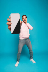 Wall Mural - handsome excited man showing pointing at empty smartphone screen posing over light blue background, 