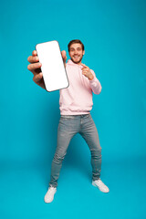 Wall Mural - handsome excited man showing pointing at empty smartphone screen posing over light blue background, 