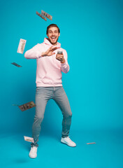 Portrait of a joyful young man holding money cash and celebrating isolated over light blue background.