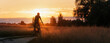 Silhouette of Cyclist rides countryside dirt road at sunset. Panoramic view.
