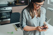 © Tijana - High angle view of happy business woman typing text message on her smartphone while standing in the kitchen